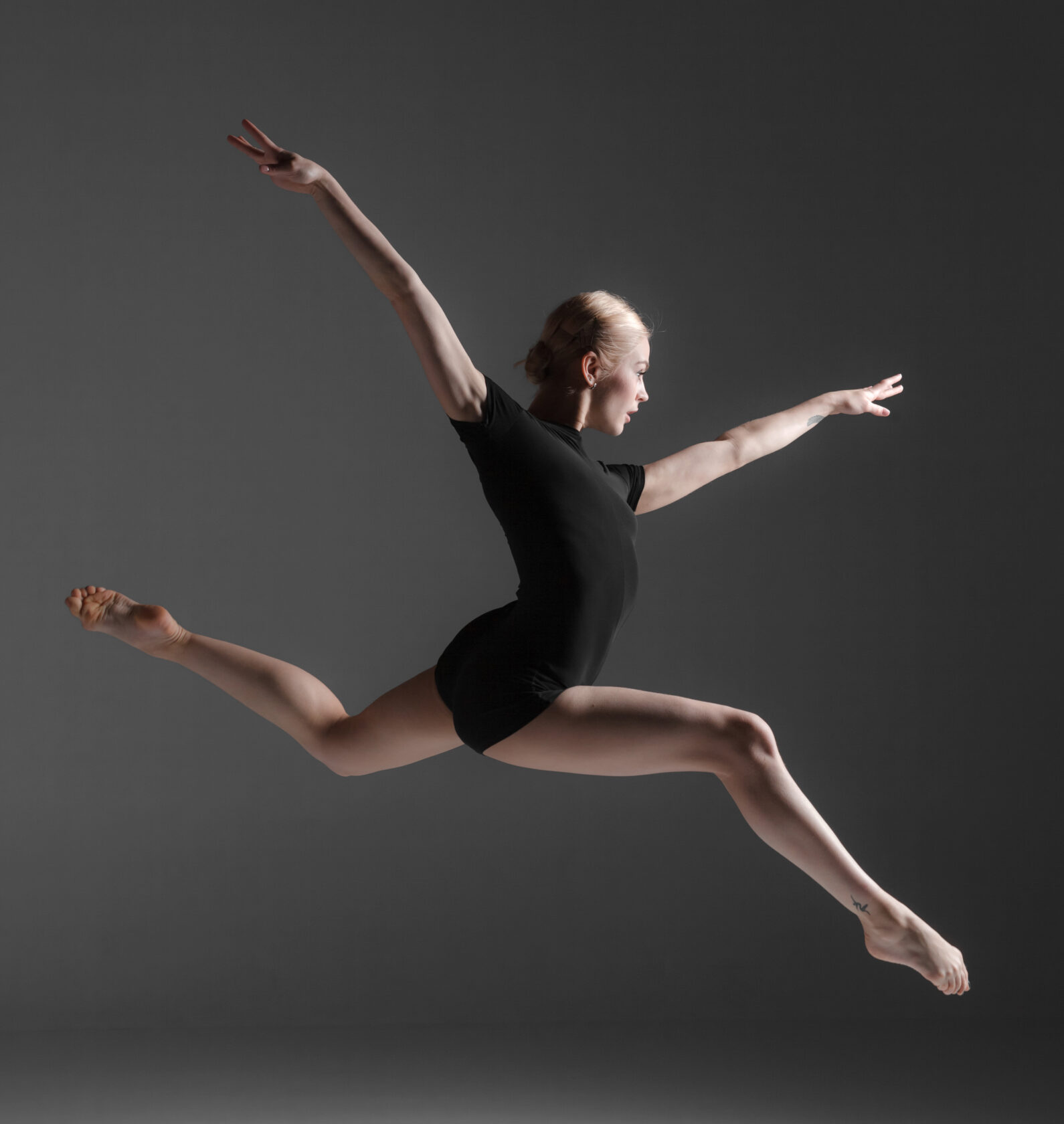 young beautiful modern style dancer jumping on a studio gray background